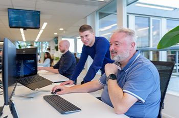 eamleden werken samen aan een computerscherm in een open kantoorruimte, met een focus op digitale productinformatie en duurzaamheid.